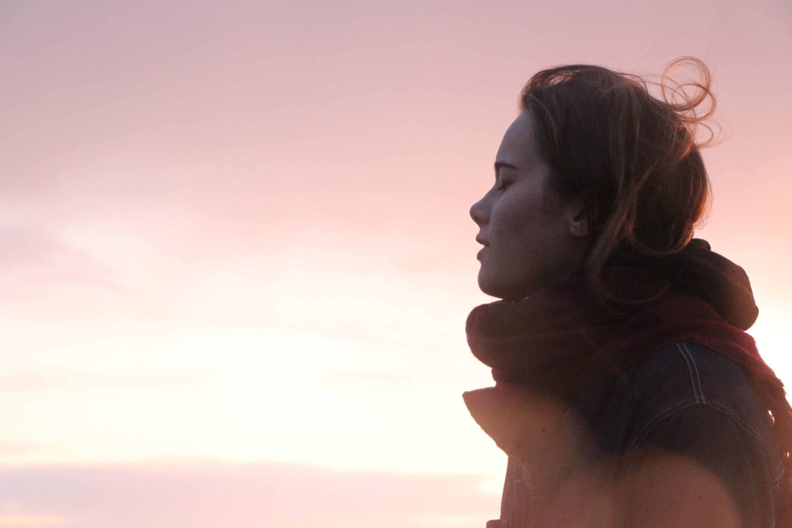 Junge Frau mit geschlossenen Augen im Sonnenuntergang – Symbolbild für achtsame Stressbewältigung